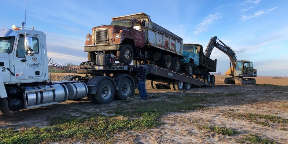 Two large dump trucks being loaded on a Grandinetti's flat bed